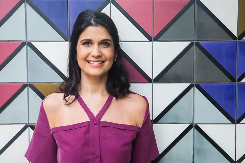 Retrato de Luiza Fecarotta sorrindo diante de uma parede de azulejos geométricos